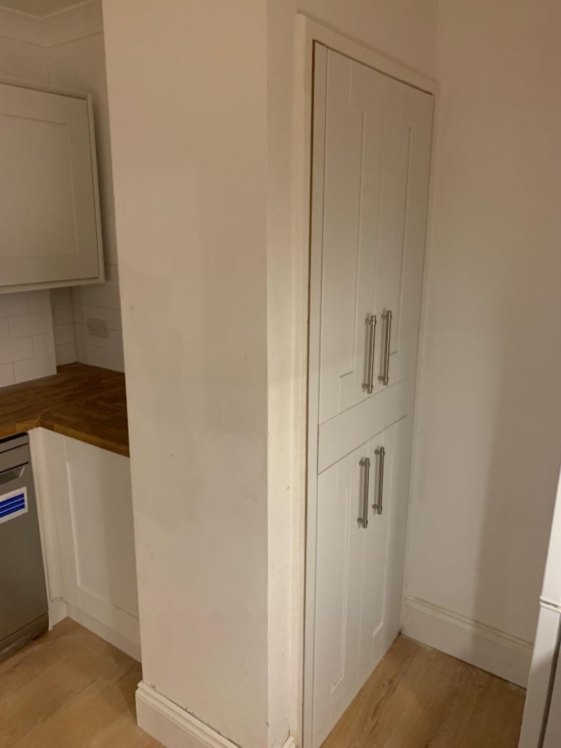 Tall fitted cupboard integrated beside a kitchen wall