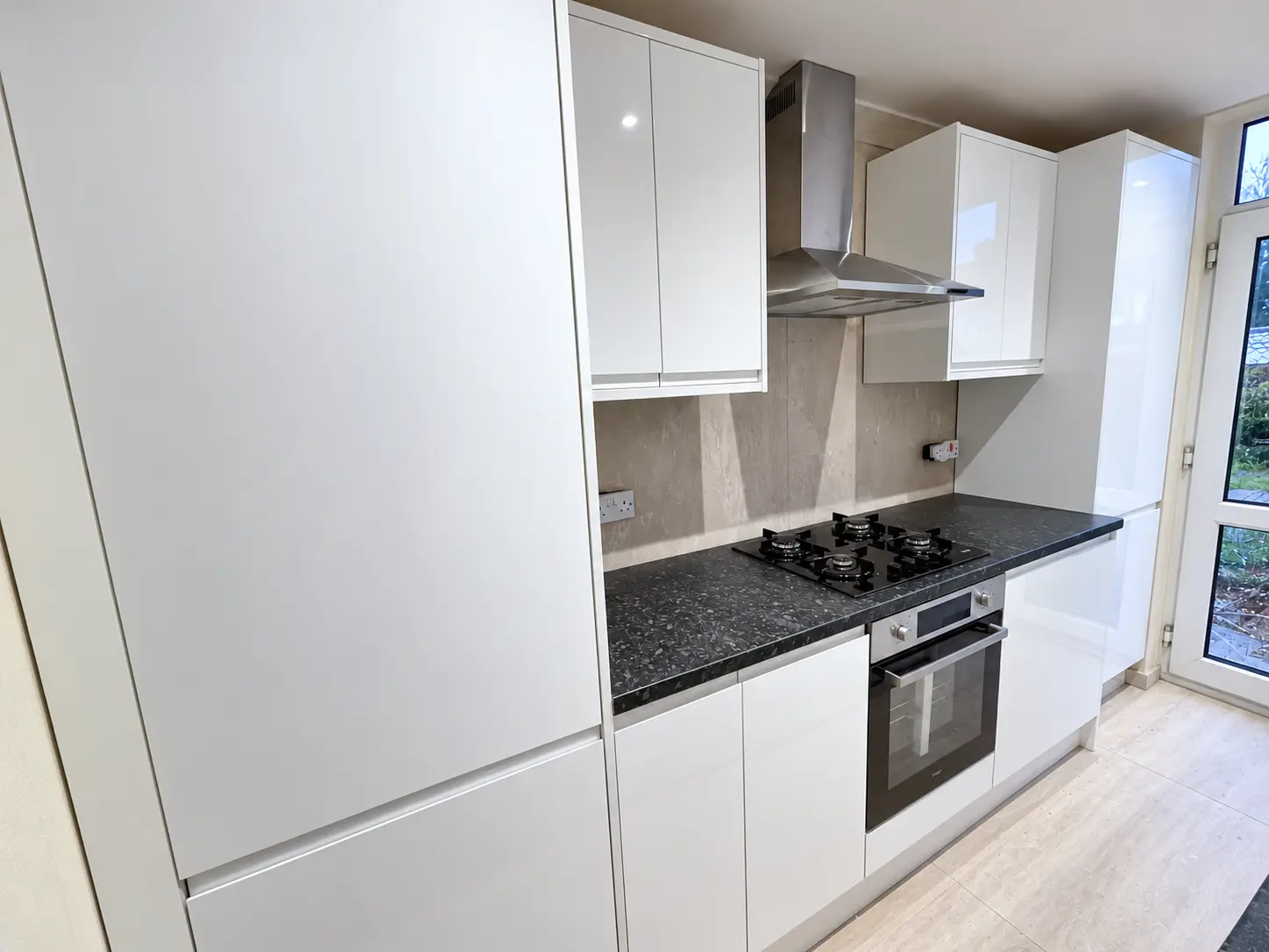 Gloss-white kitchen units with black worktop, hob, oven and extractor