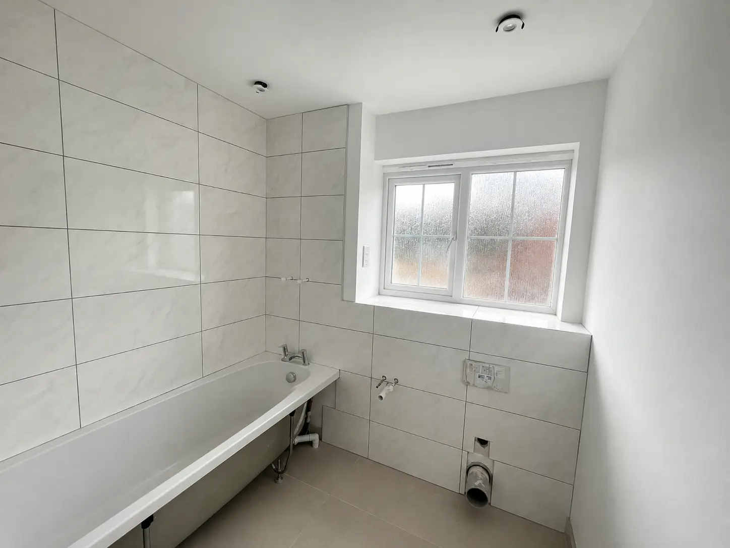 Clean bath area during fit-out with large-format wall tiles, exposed services and unfinished subfloor
