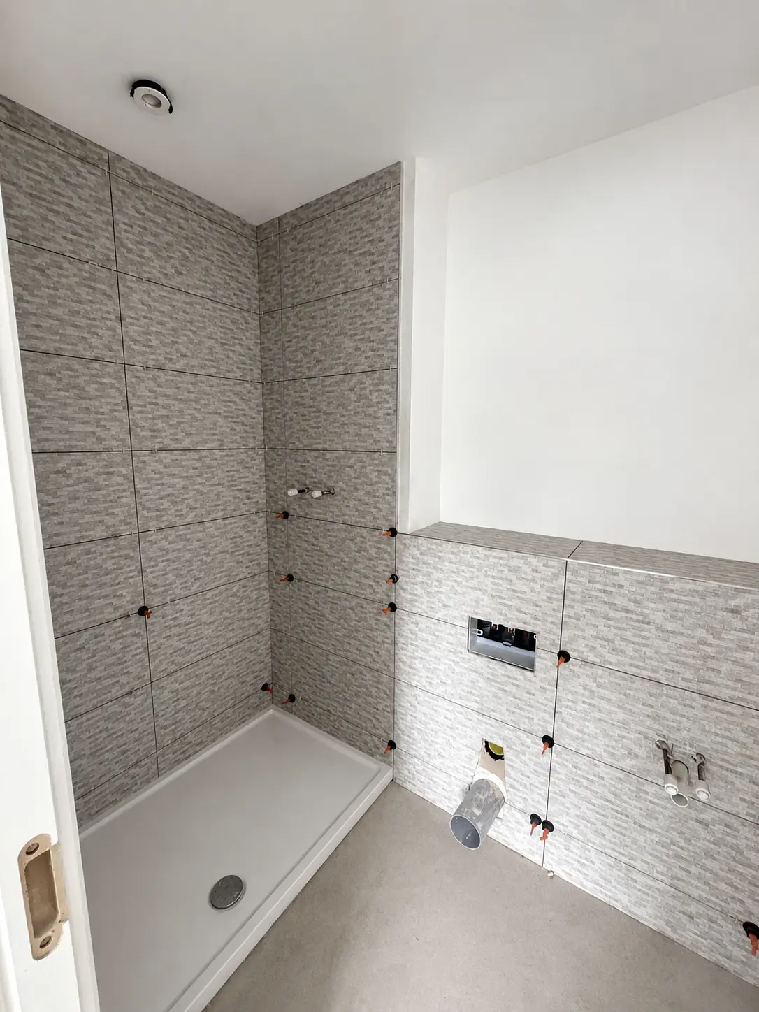 Clean shower area during fit-out with textured wall tiles, tile spacers and exposed service connections